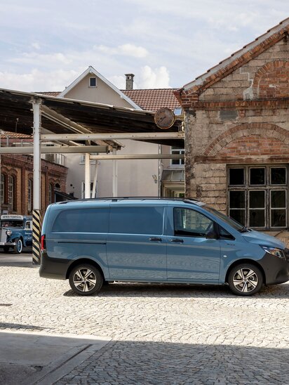 Ein blauer Mercedes-Benz eVito Kastenwagen steht vor einem alten Fabrikgebäude auf einem gepflasterten Hof. | © Mercedes-Benz AG