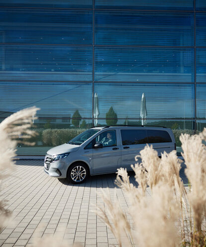Silberner Mercedes-Benz eVito Tourer parkt vor einem großen, verglasten Gebäude. | © Mercedes-Benz AG