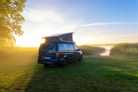 Ein blauer Mercedes-Benz Marco Polo mit Aufstelldach parkt auf einer Wiese am Ufer eines Sees im Morgenlicht. | © Mercedes-Benz AG