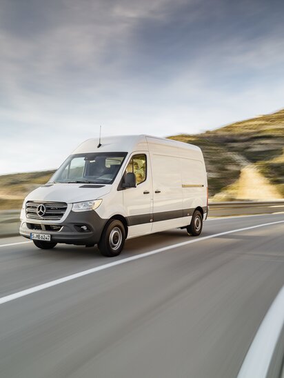 Ein weißer Mercedes-Benz Sprinter Kastenwagen fährt auf einer Landstraße.