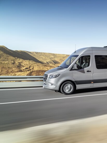 Ein silberner Mercedes-Benz Sprinter Tourer fährt auf einer kurvigen Straße durch eine Wüstenlandschaft.