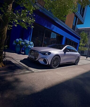Mercedes-Benz Auto parkt auf einer städtischen Straße vor einem blauen Gebäude, umgeben von Pflanzen. | © Mercedes-Benz AG