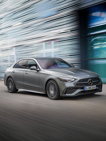 Eine graue Mercedes-Benz C-Klasse Limousine fährt dynamisch vor unscharfem Hintergrund.
