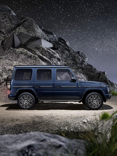 Seitenansicht einer blauen Mercedes-Benz G-Klasse vor felsiger Kulisse bei Nacht.